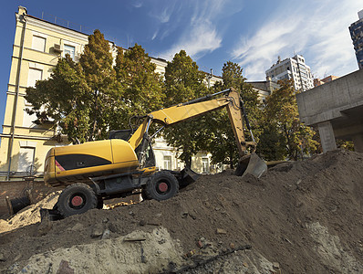 在修建公路和一座新的多层楼期间建造重型建筑挖土机时使用的挖掘机活动多层街道压力车轮服务修理操作拖拉机车道图片