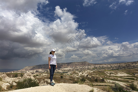 一个年轻女孩站在卡帕多西亚的岩石上 考察周围空间与蓝色云层和山地景色的关系图片