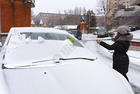 一位年轻女子从车的表面打扫雪图片