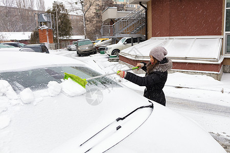 年轻女子从车的表面打扫雪图片