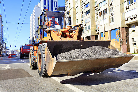 一名道路工人在修路时用重型建筑推土机桶装碎石图片