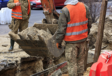 公路工人环绕着一桶重型建筑挖土机 在修筑公路上的城市下水道时挖掘沟渠图片