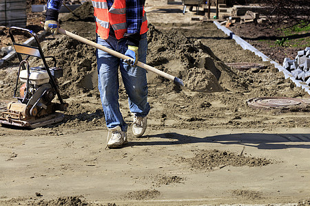 工人在人行道上铺地砖时 背着建筑铲子沙堆把地基夷平图片