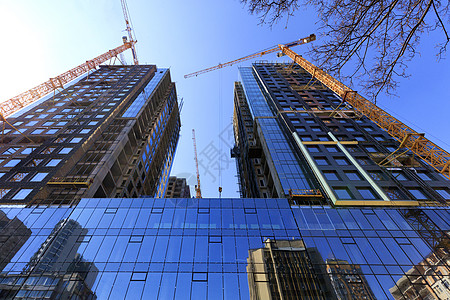 玻璃面罩 蓝色天空和起重机的反射物 在一座正在建造的现代混凝土大楼附近图片