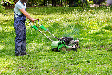 一名穿蓝制服的工人用工业汽油割草机切绿草图片