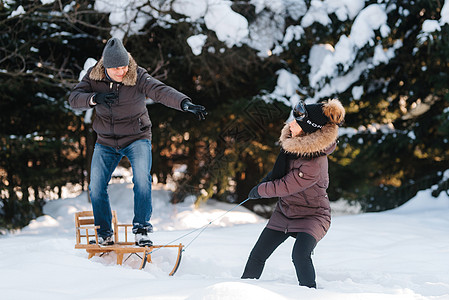 男孩和女孩户外冬季散步玩雪球雪橇夹克绿色白色幸福雪堆太阳喜悦院子树木图片