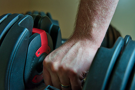 在家工作时手握着可调适的哑铃 男人手戴戒指 能看得见健身房训练钟声锻炼健身体能体质家庭权重重量图片