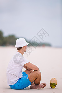 热带度假期间喝椰子奶的年轻女子海洋女士享受微笑太阳镜支撑晴天蓝色海滨帽子图片