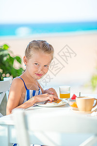 可爱的小女孩早上一大早在咖啡馆吃早餐 海景如海孩子幸福童年咖啡店勺子酒店海洋食物餐厅盘子图片