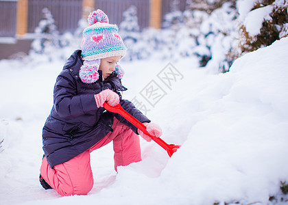 可爱的小女孩在冬日玩雪铲雪游戏女性季节手套晴天森林快乐幸福雪堆微笑童年图片