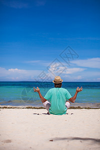坐在白色热带海滩莲花位上的年轻男青年海岸成人假期冥想沉思海洋精神男性蓝色快乐图片