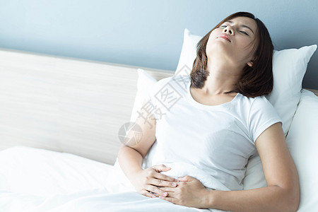 躺在白床上的近身妇女胃痛 保健问题白色女性疼痛腹部痛苦经期便秘腹痛图片