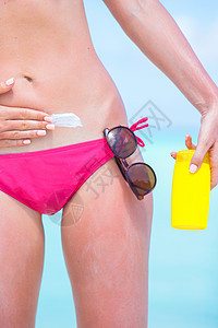 年轻女子在白沙滩上用防晒霜胃女孩瓶子棕褐色晴天比基尼海滩日光浴防晒泳装假期图片