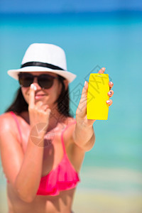 年轻快乐的女士 在白沙滩上的鼻子上涂防晒霜日光浴紫外线旅行晴天海滩瓶子棕褐色泳装防晒系数图片