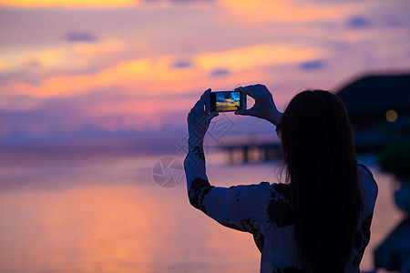 女人在她美丽的日落的手机上拍照假期橙子日出荒野电话场景棕榈照片热带闲暇图片