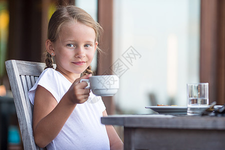 可爱的小女孩 在户外咖啡厅早餐时喝茶果汁女孩女儿水果微笑金发桌子小吃餐厅快乐图片