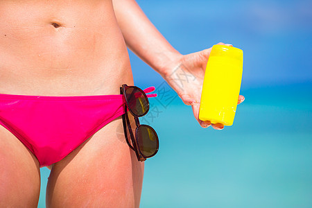 年轻女子在白沙滩上用防晒霜申请防晒皮肤护理游泳衣蓝色棕褐色旅行海滩女性女士图片