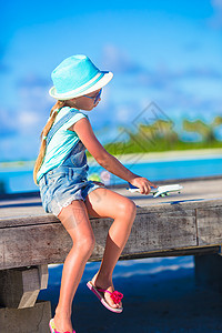 带着玩具飞机的快乐小女孩 在白沙滩上手握着玩具飞机游戏孩子眼镜黄色工艺假期翅膀航班童年手工图片