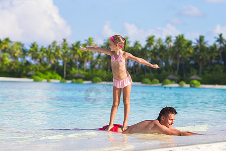小女孩在海滩上练习冲浪 在她爸爸身上父亲孩子冒充海浪女孩海洋女儿海岸泳装乐趣图片
