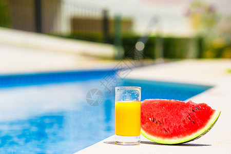 夏季和新鲜主题 红成熟的西瓜和靠近游泳池的橙汁杯子图片