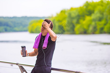 青年运动员在户外慢跑后带毛巾和瓶水男人静音锻炼液体净化瓶子音乐健康运动训练图片