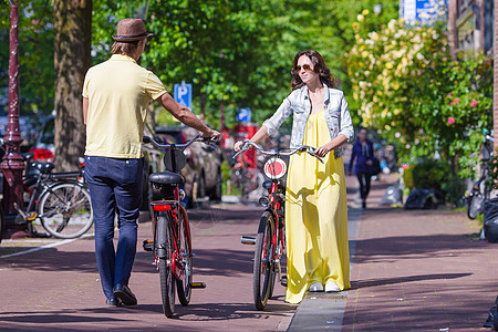 在荷兰阿姆斯特丹老街上骑自行车的年轻快乐夫妇城市男人首都社论游客中心历史运输运河反射图片