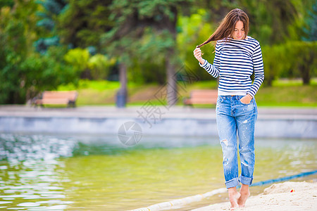 年轻快乐的女子在温暖秋天靠近湖边走来走去女士晴天头发发型魔法赤脚女性潮人草地牛仔裤图片