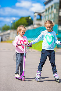 两个小女孩滑溜溜溜溜 骑着摩托车在公园露天微笑乐趣女性闲暇头盔幸福滑冰姐姐滚筒喜悦图片