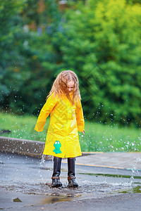 穿雨衣和靴子的小女孩 在户外的雨中玩图片