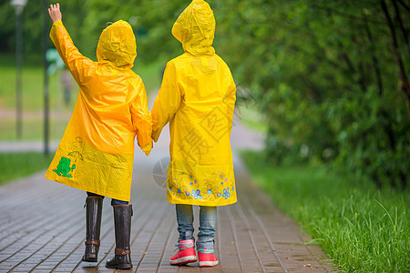 在温暖秋天的雨下 可爱的小姑娘们外套水坑孩子预报雨衣公园季节风暴下雨飞溅图片