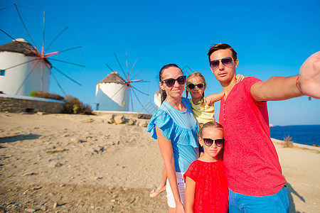 四口四口自拍的家庭 在希腊米科诺斯岛热门旅游区风车前拿着棍子图片