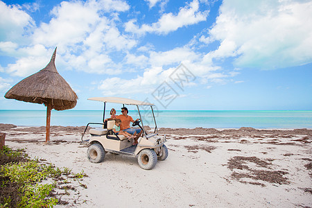 在热带海滩带父亲高尔夫车的小女孩姐妹海岸线海景微笑高尔夫球车辆孩子闲暇天空支撑图片