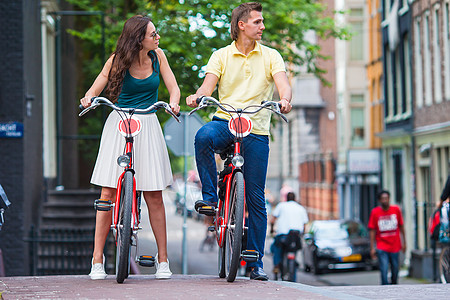 在阿姆斯特丹老街上骑自行车的 年轻快乐的夫妇男人女士运输历史性中心旅游运河城市旅行街道图片