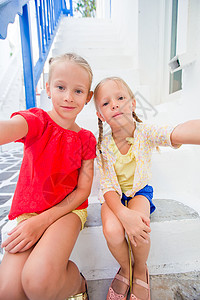 两个穿蓝裙子的女孩在Mykonos街上 户外玩得开心窗户女儿房子教会村庄自拍街道城市建筑蓝色背景图片