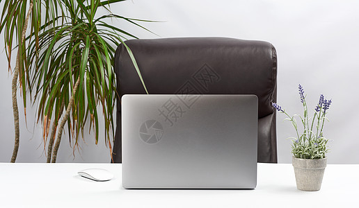 一个开着的灰色笔记本电脑站在白桌子上 紧靠一根铁丝线图片