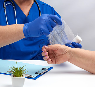 医生坐在一张蓝色制服和乳胶手套的桌子上拇指帮助手臂援助疾病保健女士情况药品手术图片