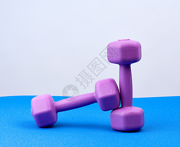 一对紫色塑料哑铃 在蓝色新胎垫上运动小地毯活动女性损失身体瑜伽健身房白色训练图片
