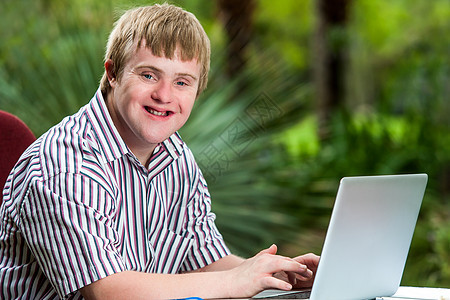 残疾青年男子在花园的笔记本电脑上打字图片