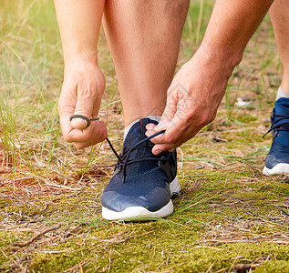 穿着黑色制服的运动员蹲着 把鞋带绑在蓝SN上跑步运动女士日落公园森林慢跑者花边蓝色男人图片