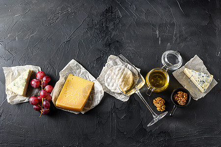 奶酪开胃菜选择或小吃套餐 黑色背景 顶视图 复制空间中的各种模制法式奶酪 葡萄 山核桃 白苏维翁葡萄酒和蜂蜜图片