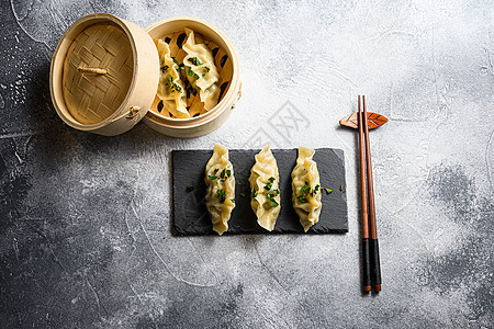 木蒸锅和黑石板上的煮热中国饺子 在灰色石头纹理的桌子背景顶视图上图片