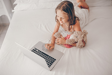 在笔记本电脑上做家庭作业的可爱小女孩女性孩子沙发键盘游戏地面快乐幸福电子邮件瞳孔图片