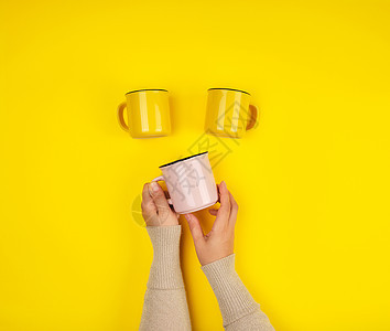 黄色背景的陶瓷杯和女性手图片