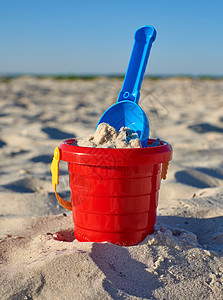 海滩上带沙和铲子的红色婴儿塑料桶晴天玩具塑料乐趣蓝色海岸闲暇童年旅行假期图片