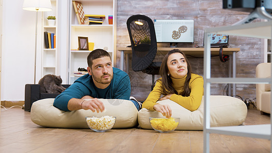 欢快的一对情侣坐在枕头上看电视夫妻家庭沙发筹码成人女士男朋友爆米花长椅地板图片