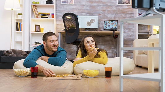 快乐的白人夫妇坐在枕头上吃披萨爆米花沙发地板女士长椅男朋友宠物夫妻电视筹码图片