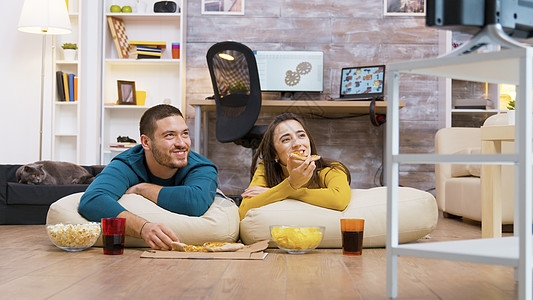 快乐的白人夫妇坐在枕头上吃披萨地板家庭长椅女士男朋友成人动物爆米花夫妻沙发图片