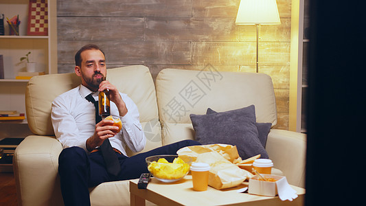 有领带的商务人士坐在沙发上吃汉堡客厅电视食物垃圾公寓程序食欲商务长椅电话图片