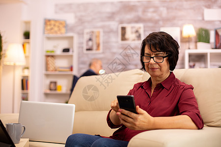 家中使用现代技术的年长妇女微笑老夫妻手机沙发成人夫妇男人幸福电脑退休图片