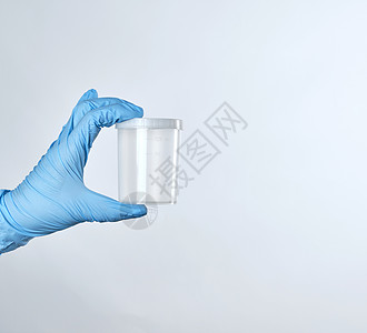 一只蓝色消菌手套手握着一个空塑料容器 用于图片